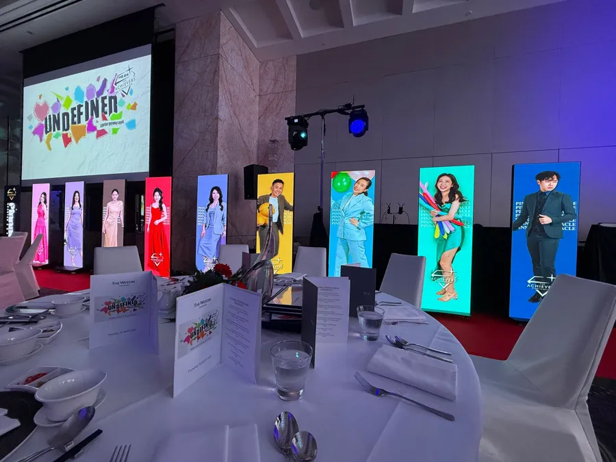 A row of LED poster stands showing guest portraits behind dinner tables